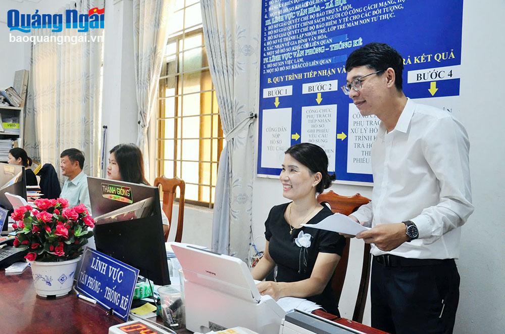 Phó Chủ tịch UBND xã Bình Dương (Bình Sơn) Nguyễn Quốc Đạt (người đứng) kiểm tra việc giải quyết thủ tục hành chính cho người dân tại bộ phận một cửa của xã. Ảnh: H.THU  